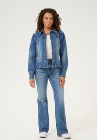 Denim jakna s svetlo modrim pranjem, klasičnim ovratnikom, gumbi na sprednji strani in dolgimi rokavi. V kombinaciji z ustreznimi širokimi kavbojkami in belimi športnimi copati.