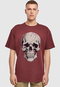 Mørkerød oversized t-shirt lavet af bomuld, med et detaljeret grafisk motiv af et kranium i kontrastfarver på forsiden. Korte ærmer.