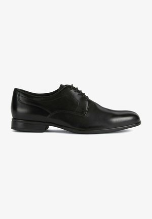 Chaussure habillée en cuir noir avec finition lisse, bout arrondi et laçage à l'avant. Présente un talon bas et un subtil détail de couture sur les côtés.
