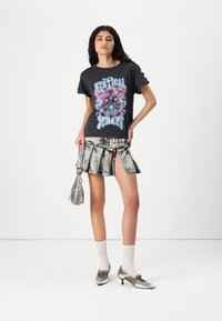 T-shirt graphique noir avec un design coloré "Rêves Mystiques". Associé à une mini-jupe en denim déchiré avec des accents métalliques. Accessoires argentés.