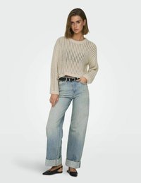 Beige Strickpullover mit offenem Maschenmuster, cropped Silhouette, kombiniert mit hellblauen weit geschnittenen Jeans mit umgeschlagenen Säumen und schwarzen Ballerinas.