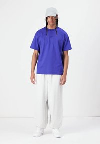 Violeta Nike t-krekls ar īsām piedurknēm, papildināts ar gaiši pelēkiem treniņbriļļiem un baltām sporta apavām. Outfits ir brīvs sasist.