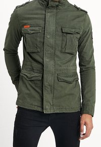 Olivgrön militärjacka i bomull med fyra överdimensionerade framfickor, ståkrage och axelband.