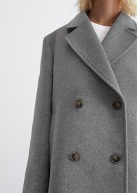 Cappotto doppio petto grigio in lana con rever, dotato di due bottoni scuri, tessuto strutturato e vestibilità rilassata.