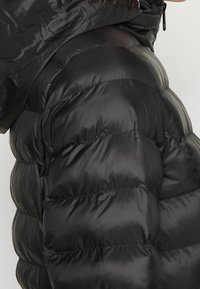 Chaqueta de plumas negra con un exterior brillante y acolchado, que cuenta con una capucha y costuras horizontales prominentes para aislamiento.