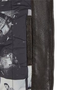 Interiorul unei jachete negre din piele, cu țesătură gri matlasată și imprimeuri fotografice monocrome. Finisaj texturat și închidere cu fermoar.