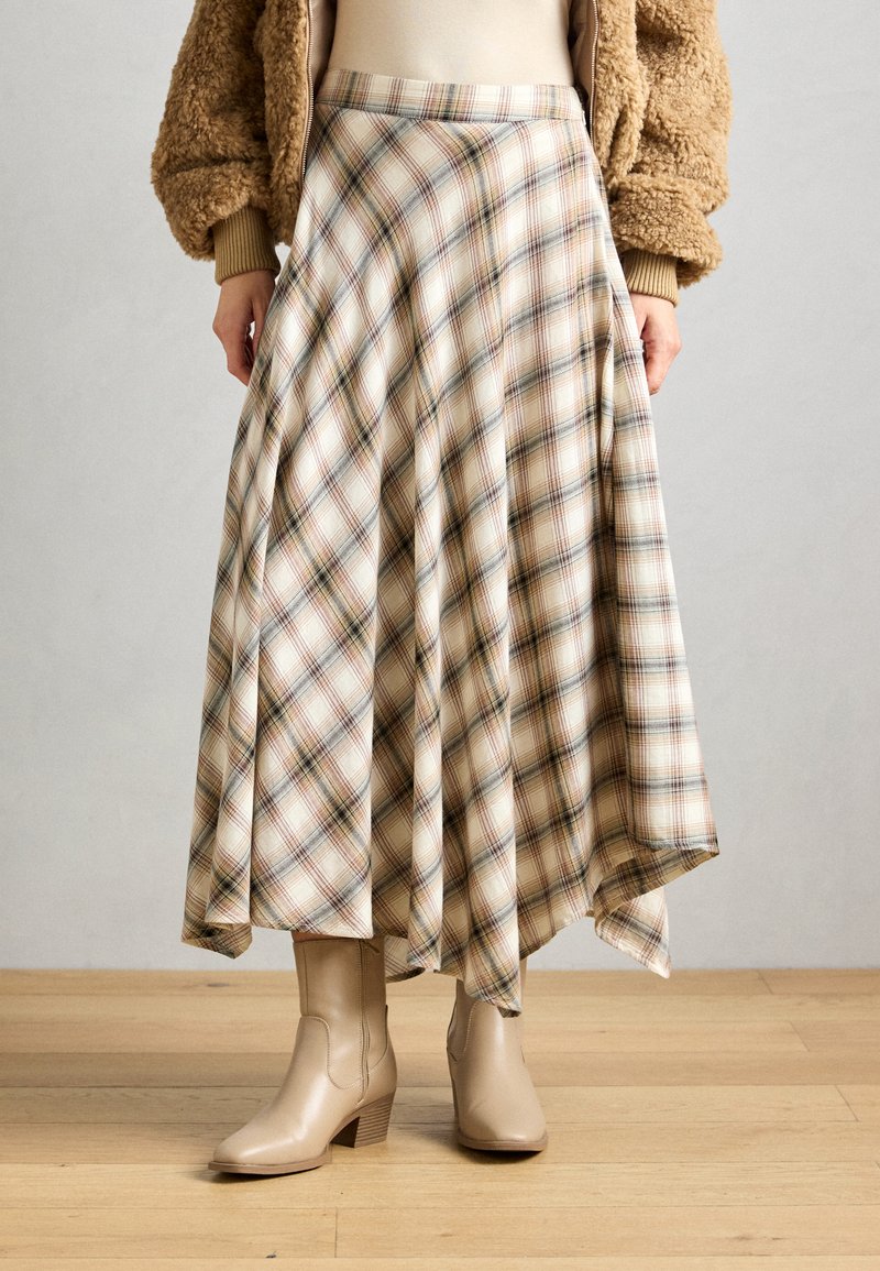 Beige ternet midi-nederdel med et flydende A-linje design, der har brune og tan linjer på en cremet baggrund. Kombineret med beige ankelstøvler.