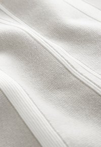 Tessuto bianco con superficie texturizzata, caratterizzato da sottili righe verticali e una cerniera liscia lungo il centro. Materiale morbido e intrecciato.