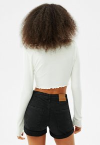 Vitt ribbat långärmat kort linne med vågig fåll, tillsammans med midjehöga svarta jeansshorts med uppvikta fållar och en brun läderlapp.