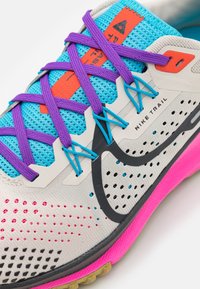 Nike trail løbesko med en grå og hvid mesh-overdel, blå og lilla snørebånd, sorte detaljer og en pink polstret sål med struktureret greb.