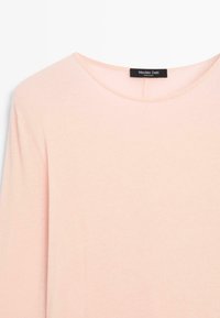 Helles rosa Langarmshirt mit rundem Ausschnitt. Der Stoff wirkt weich mit einer glatten Textur. Hat ein schwarzes Etikett am Nacken.