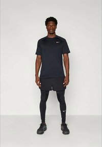 Svart treningst-skjorte fra Nike med korte ermer og en rosa logo, parret med svarte shorts og tettsittende leggings, komplementert med svarte joggesko.