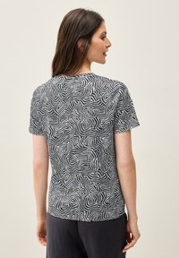T-shirt à manches courtes à motif noir et blanc avec un design de lignes ondulées. Tissu doux et coupe décontractée. Encolure ronde et ourlet simple.