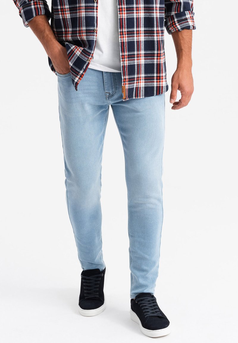 Jeans skinny bleu clair en denim, avec une finition délavée. Associés à une chemise à carreaux et des baskets noires.