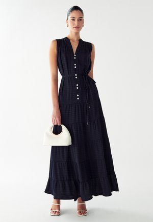 Maxi kjole i mørkeblå. Har knaplukning foran, bånd i taljen og tekstureret lagdelt stof. Sammen med en hvid buet håndtaske.