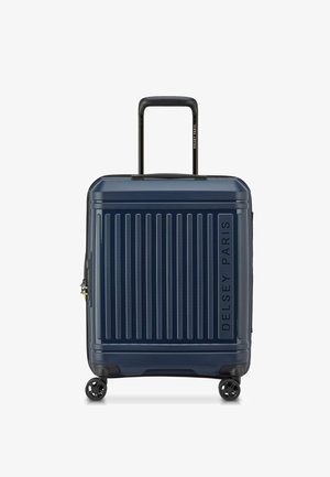 Maleta dura navy con surcos verticales, asa retractable negra, cuatro ruedas y el logo de Delsey Paris grabado en el lateral.