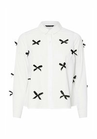 Camicia bianca a maniche lunghe con numerosi piccoli fiocchi neri sparsi sul tessuto, dotata di colletto classico e chiusura con bottoni.