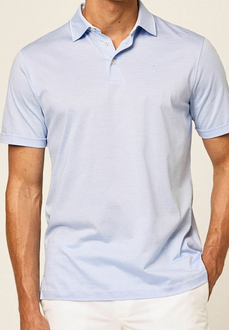 Polo bleu clair en tissu doux, avec un col classique, une patte de boutonnage à trois boutons et des manches courtes avec des ourlets à revers.