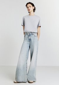 T-shirt grigio a maniche corte abbinato a jeans a gamba larga di un leggero blu chiaro con orlo grezzo e un leggero sbiadimento, completato con calzature semplici.