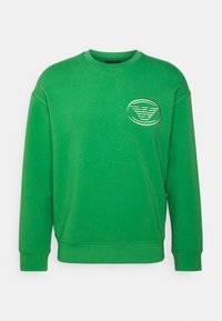 Felpa verde a girocollo con maniche lunghe e una piccola toppa ovale con ali e lettere sul petto.