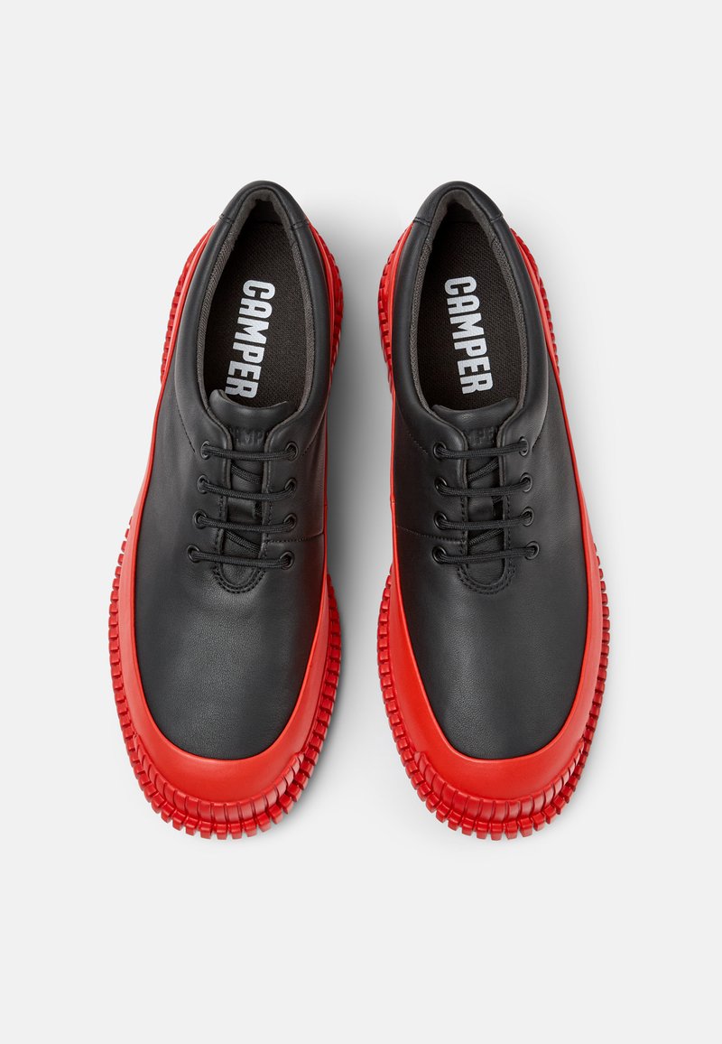 Zapatos de cuero negros con una suela de goma roja, con puntera redondeada, diseño con cordones y acentos de goma texturizada.