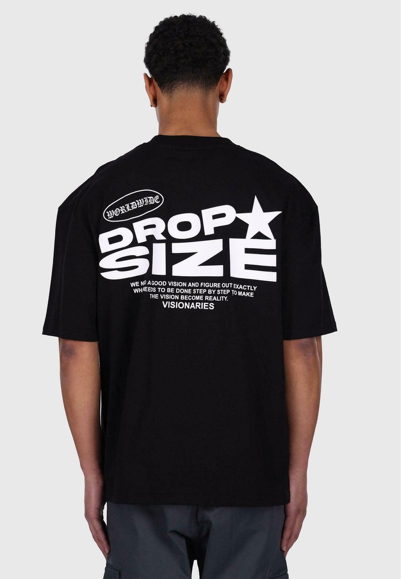 Svart bomullsoverdimensjonert t-skjorte med stor hvit tekst på ryggen, inkludert "DROP SIZE" og en stjernegrafikk. Korte ermer, avslappet passform.