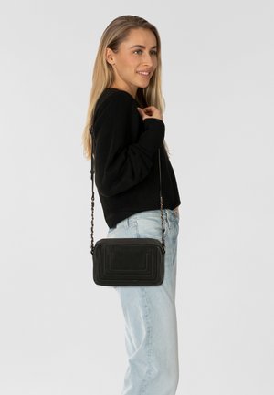 Borsa a tracolla in pelle nera con motivi trapuntati, tracolla a catena e chiusura con zip. Forma rettangolare compatta, design minimalista.