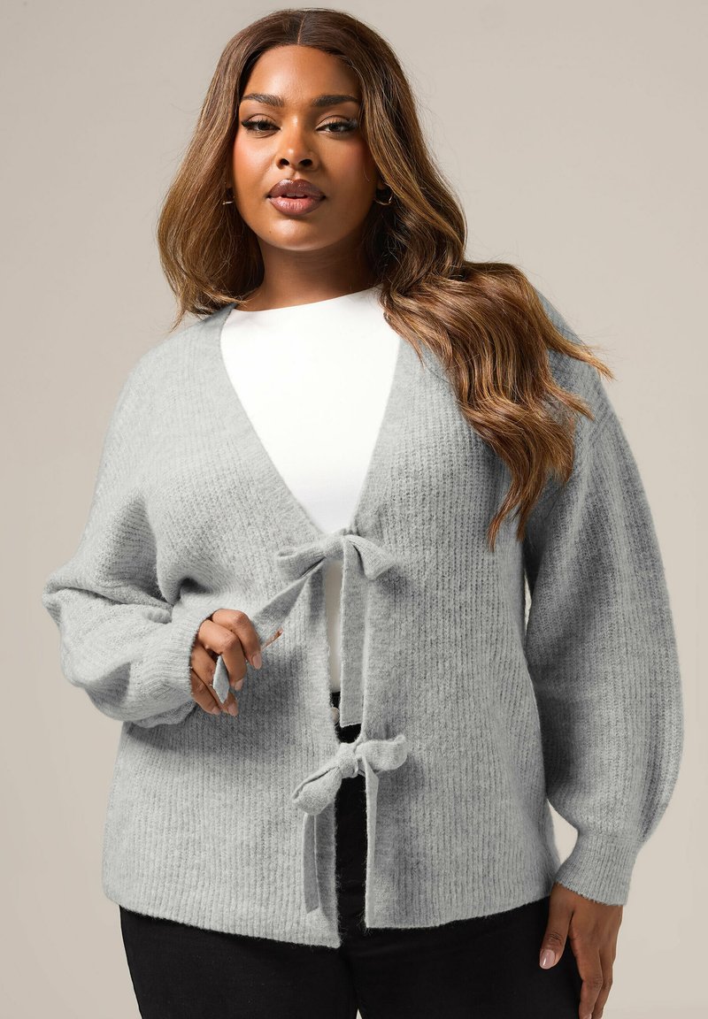 Gray knit cardigan featuring a deep V-neck, wide sleeves, and a tie closure at the front. Soft texture with a ribbed pattern throughout.