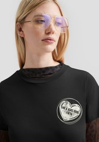 Schwarzes Baumwoll-T-Shirt mit einem runden weißen Grafikdesign, das ein Herzmotiv und Text zeigt. Glattes Material und kurze Ärmel, mit Rundhalsausschnitt.