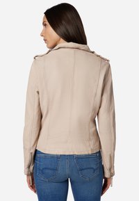 Beige läderjacka med dragkedjeslut och axelklaffar, med en figursydd design och detaljerad sömnad på ryggen.