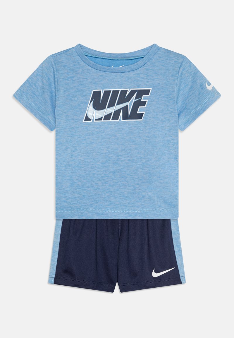 Mėlyna trumpomis rankovėmis marškinėliai su storu juodu "NIKE" logotipu, derinami su tamsiai mėlynomis šortais, kurių apatine dalimi puošia balta "Nike" veliūra.