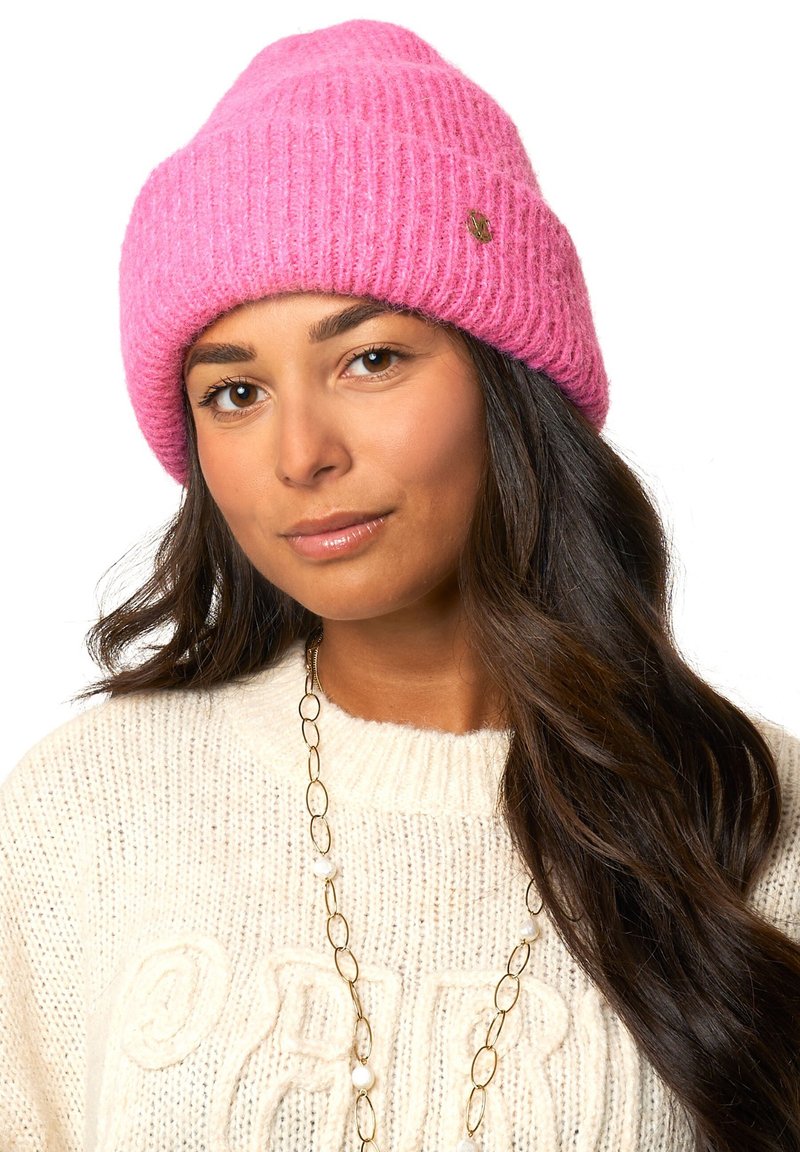 Różowa, prążkowana czapka z dzianiny wykonana z miękkiego materiału, z małym metalicznym logo. Noszona z kremowym swetrem i złotym naszyjnikiem.