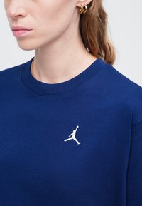 Granatowa bluza z bawełny, z okrągłym dekoltem i białym logo Jumpman wyhaftowanym po lewej stronie klatki piersiowej.