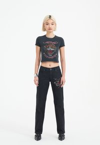 Black cropped t-shirt with a tiger graphic, paired with dark denim pants featuring colorful embroidered designs and a straight-leg cut.