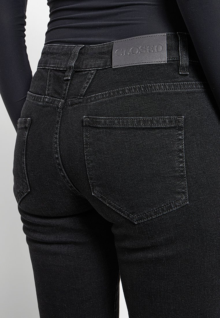 Schwarze Denim-Jeans mit schlankem Schnitt, ausgestattet mit einem Leder-Logo-Patch am Bund und klassischen Gesäßtaschen, ohne sichtbare Abnutzungserscheinungen.