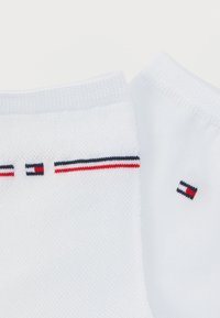 Λευκές βαμβακερές κάλτσες με ριμπ κορυφές. Διαθέτουν κόκκινο, λευκό και μπλε ριγέ μοτίβο κατά μήκος του πάνω άκρου και ένα μικρό λογότυπο κοντά στο τελείωμα.