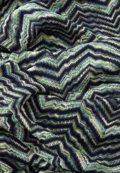 Tissu tricoté doux avec un motif chevron dans des nuances de bleu, vert, noir et blanc, montré en gros plan avec des plis et une texture.