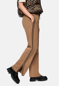 Brown sweatpants with black side stripes, featuring a leopard print accent at the cuffs. Paired with black platform shoes for contrast.