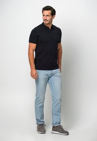 Marinblå pikétröja med korta ärmar kombinerad med ljusblå jeans och grå sneakers. Pikétröjan har en klassisk krage och två knappar.