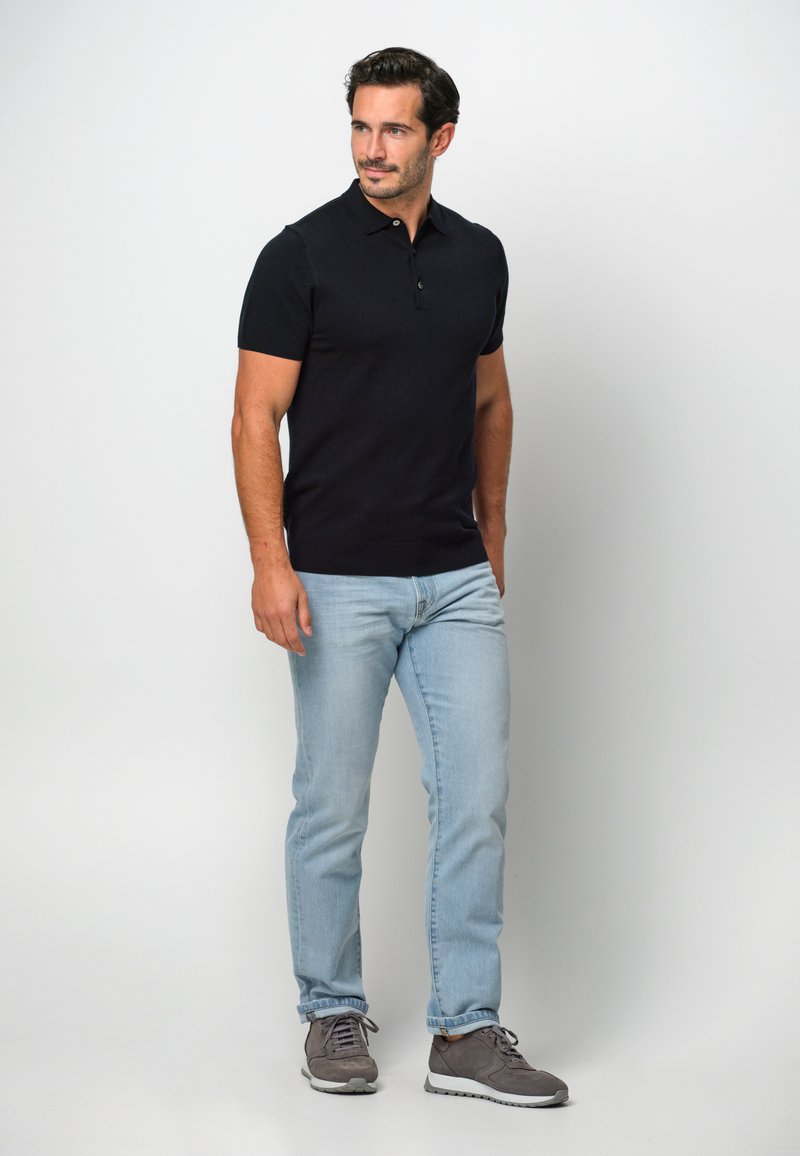 Marinblå pikétröja med korta ärmar kombinerad med ljusblå jeans och grå sneakers. Pikétröjan har en klassisk krage och två knappar.