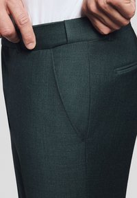 Ciemnozielone spersonalizowane spodnie z chropowatym wykończeniem, z płaskim przodem, skośnymi kieszeniami i wąskim pasem dla smukłego wyglądu.