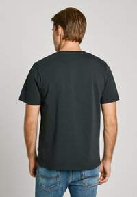 Camiseta de algodón negra con mangas cortas y cuello redondo. Presenta una textura suave y un diseño simple sin gráficos. Combinada con jeans azules.