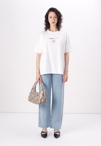 T-shirt branca de algodão com gráfico impresso, jeans azul claro com detalhes brilhantes e uma bolsa estampada. Sapatilhas pretas completam o visual.