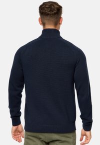 Marineblå striktrøje med høj hals, ribbede manchetter og kant; har en glat tekstur og tætsiddende design.