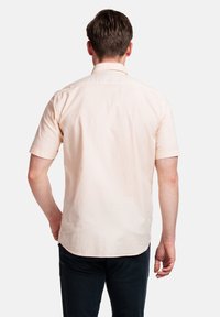 Korte mouwen, licht perzikkleurig overhemd met knopen, een soepele textuur, een gebogen zoom en zichtbare stiksels. Draag het met een donkere broek.