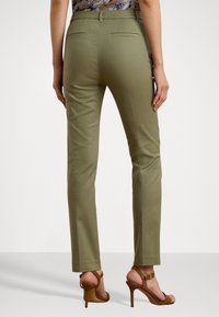 Olivgröna skräddarsydda byxor med en slät yta, slim-fit design och bakfickor. Matchas med bruna högklackade sandaler.