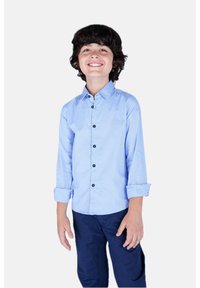 Camicia azzurra chiara a maniche lunghe con chiusura a bottoni, polsini ripiegati e bottoni scuri. Indossata con pantaloni blu navy. Design semplice, senza motivi.
