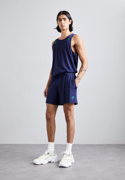 Marine blå idrettstopp og shorts laget av pustende stoff. Har grønne aksenter og en logo. Kombinert med hvite joggesko og sokker.