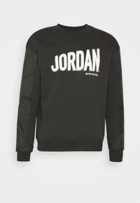 Sweat-shirt noir avec "JORDAN" en lettres blanches épaisses, doté d'un tissu lisse, de manches brillantes contrastantes, d'un col rond et de poignets côtelés.