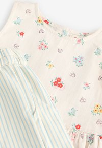 Gros plan sur une robe de couleur claire à petits motifs floraux et cœurs, associée à un pantalon à rayures bleu clair et blanc.